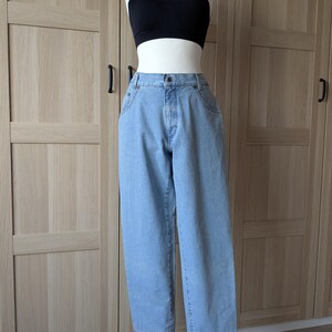 Könnte beinhalten: Hellblaue Jeans und ein schwarzes Crop-Top auf einer Schaufensterpuppe. Die Jeans hat eine hohe Taille und eine lockere Passform. Das Crop-Top ist einfarbig schwarz. Die Schaufensterpuppe steht auf einem Holzständer.
