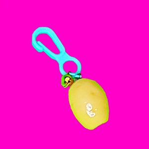 May include: A light blue plastic clip attached to a small, yellow, pear-shaped object.
