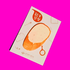Può includere: Un foglio appiccicoso bianco con un'illustrazione di cartone animato di una fetta di pane. La nota ha il testo "STICKY NOTE" e i caratteri cinesi "早餐" e "能吃" in arancione.