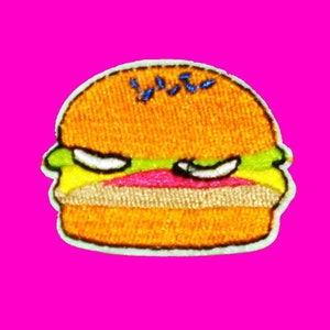 May include: A yellow, green, and pink embroidered patch of a cartoon burger with an angry expression.