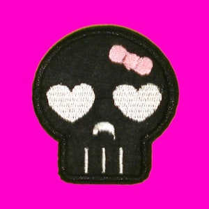 May include: Black embroidered skull patch with white heart eyes and a pink bow.