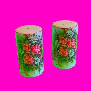 Puede incluir: Un par de saleros y pimenteros de cerámica blanca con un diseño floral. Los saleros tienen un fondo verde con flores rosas, naranjas y amarillas.