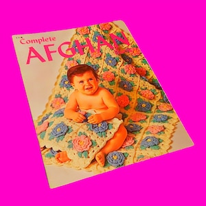 May include: A vintage crochet pattern book cover featuring a baby girl sitting on a crocheted blanket with floral designs in shades of pink, blue, and yellow. The cover reads "Complete Afghan".