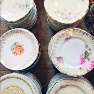 May include: A stack of vintage floral patterned plates with gold trim. The plates are in various sizes and feature different floral designs.
