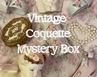 May include: A collection of decorative items including a ceramic angel figurine, a gold-toned oval box, a string of white pearls, a ceramic shoe, and several napkin rings with pink rose accents. The text Vintage Coquette Mystery Box is visible.