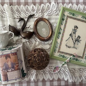 May include: An assortment of vintage items including a white teacup, a bronze swan figurine, a framed illustration, a decorative box, a small oval frame, a floral spoon, and a Lipton's Tea tin.