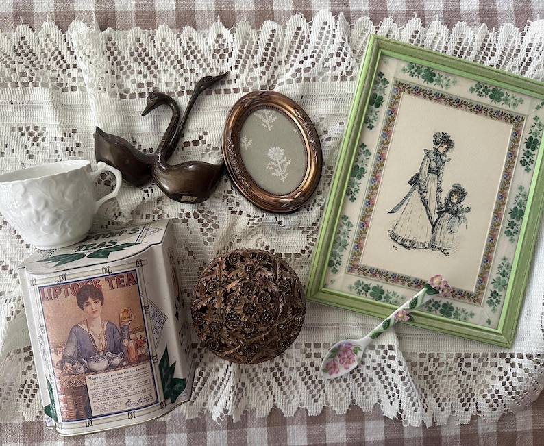 May include: An assortment of vintage items including a white teacup, a bronze swan figurine, a framed illustration, a decorative box, a small oval frame, a floral spoon, and a Lipton's Tea tin.