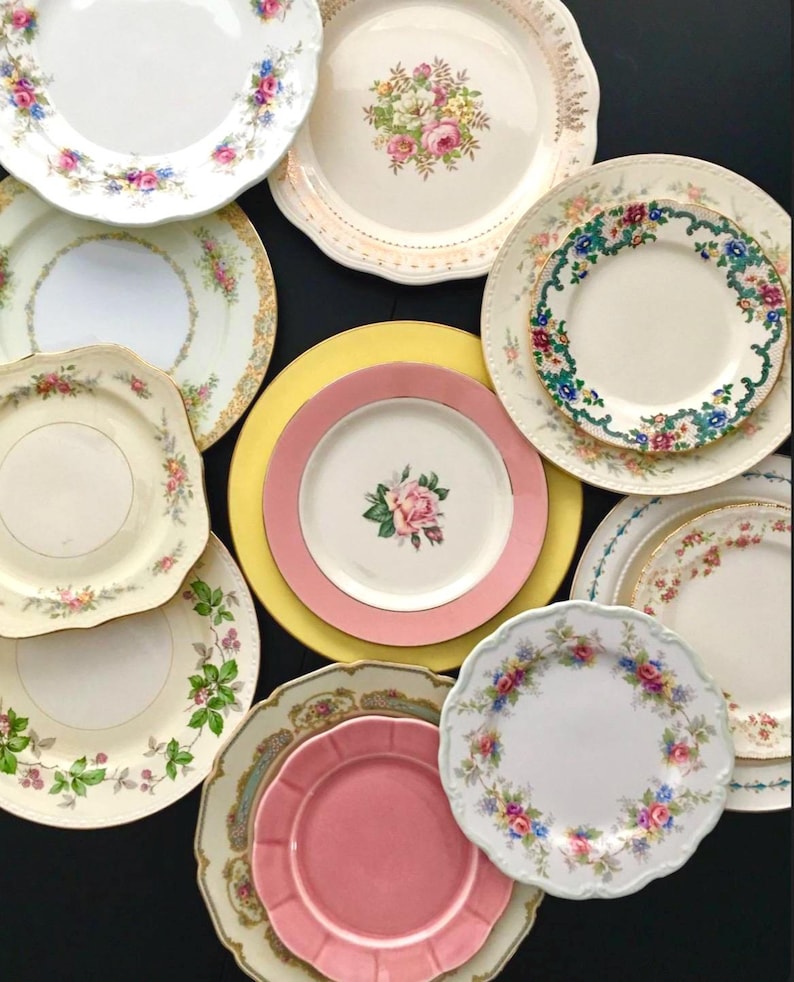 May include: A collection of vintage floral patterned plates in various sizes and colors, including pink, yellow, and white. The plates are arranged in a circular pattern on a black background.