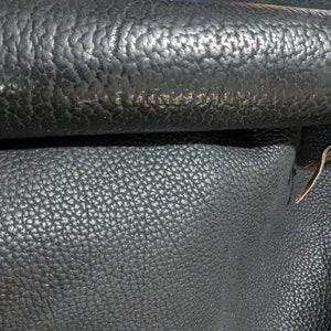 May include: Close-up of black leather with a textured surface. The leather has a pebbled grain pattern.
