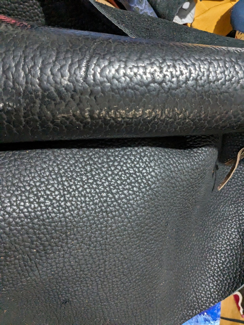 May include: Close-up of black leather with a textured surface. The leather has a pebbled grain pattern.