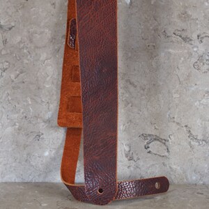 May include: A brown leather guitar strap with a suede patch and adjustable length.