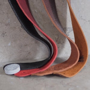 May include: Four leather straps in different colors, including black, red, brown, and tan, are arranged in a curved shape. The straps are all the same width and have a smooth, textured surface.