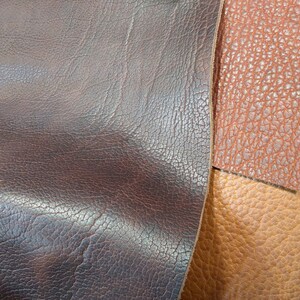 May include: Close-up of three different types of leather. The leather is brown, tan, and dark brown. The leather has a textured surface.