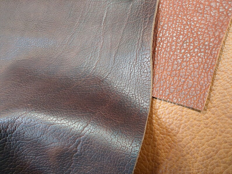 May include: Close-up of three different types of leather. The leather is brown, tan, and dark brown. The leather has a textured surface.