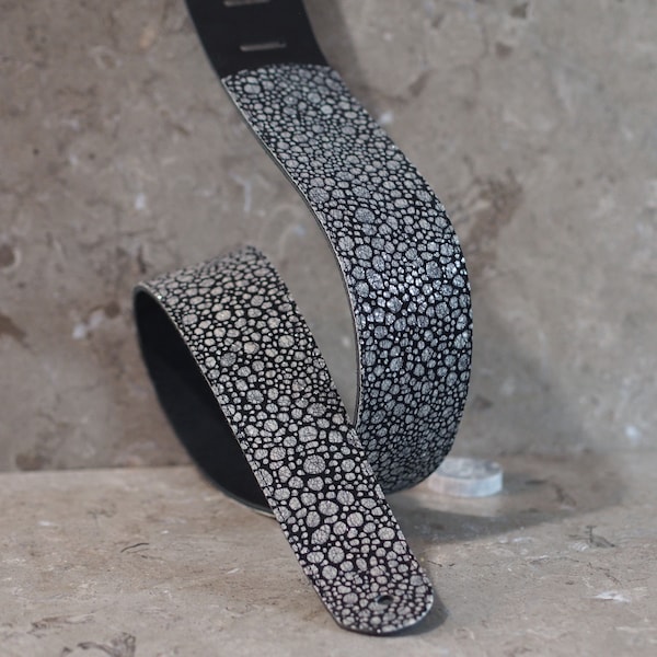 Manchas blancas crujientes sobre correa de guitarra de cuero negro