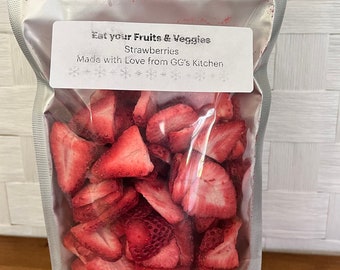 May include: A clear plastic bag filled with dried strawberry slices. The bag has a white label that reads "Eat your Fruits & Veggies Strawberries Made with Love from GG's Kitchen".
