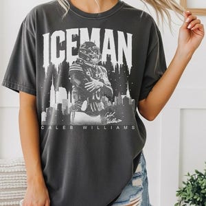 May include: Dark gray t-shirt featuring the word "ICEMAN" above a black and white image of a football player in a helmet, with a cityscape silhouette. The player's name, Caleb Williams, is printed below the image.