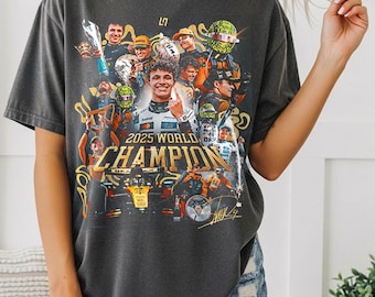May include: Dark gray t-shirt featuring a colorful graphic with the text "2025 WORLD CHAMPION". The graphic includes images of race car drivers and race cars. The shirt is a Pepper Comfort Colors 1717.