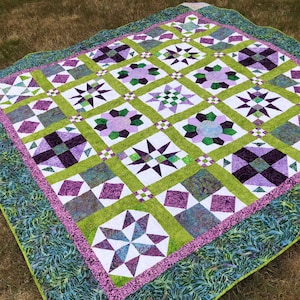 May include: A quilt with a patchwork design featuring a variety of geometric shapes in shades of green, purple, and white. The quilt is made with a variety of fabrics, including floral prints and solid colors.