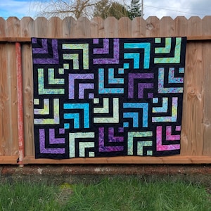 A colorful log cabin quilt hanging on a fence outdoors