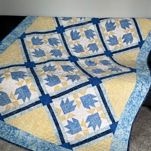 May include: A handmade quilt with a bear paw pattern. The quilt features a repeating pattern of blue bear paw shapes on a white background, framed by yellow squares and blue borders. The quilt is made of soft fabric.