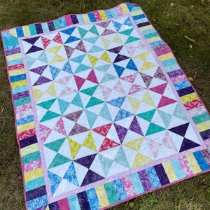 May include: A rectangular quilt featuring a patchwork design of multi-colored triangles in shades of pink, yellow, blue, purple, and green, interspersed with white triangles. The border consists of vertical fabric strips in matching colors.