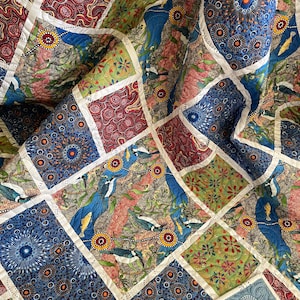 May include: A patchwork quilt featuring a variety of colorful square patterns. The quilt showcases designs with birds, floral motifs, and abstract patterns in shades of blue, red, green, and brown. White stitching outlines each square, creating a textured effect.