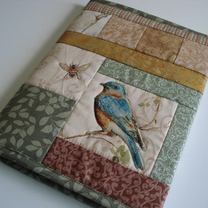 May include: A patchwork fabric book cover with a bluebird and a bee design. The cover is made of different fabrics with floral patterns and a green leafy pattern.