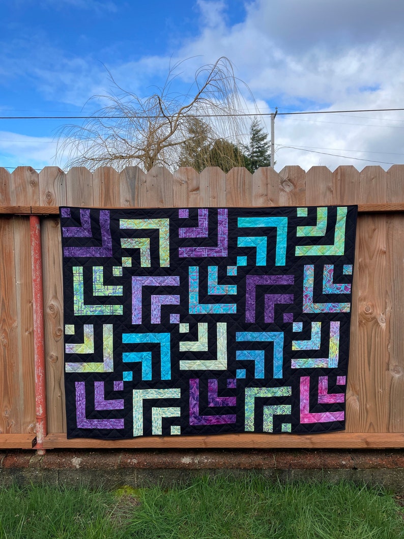 A colorful log cabin quilt hanging on a fence outdoors