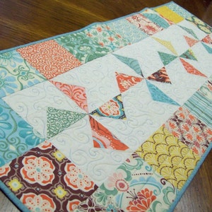 May include: A blue and white table runner with a patchwork design featuring various floral patterns. The runner is made of fabric squares sewn together in a geometric pattern.