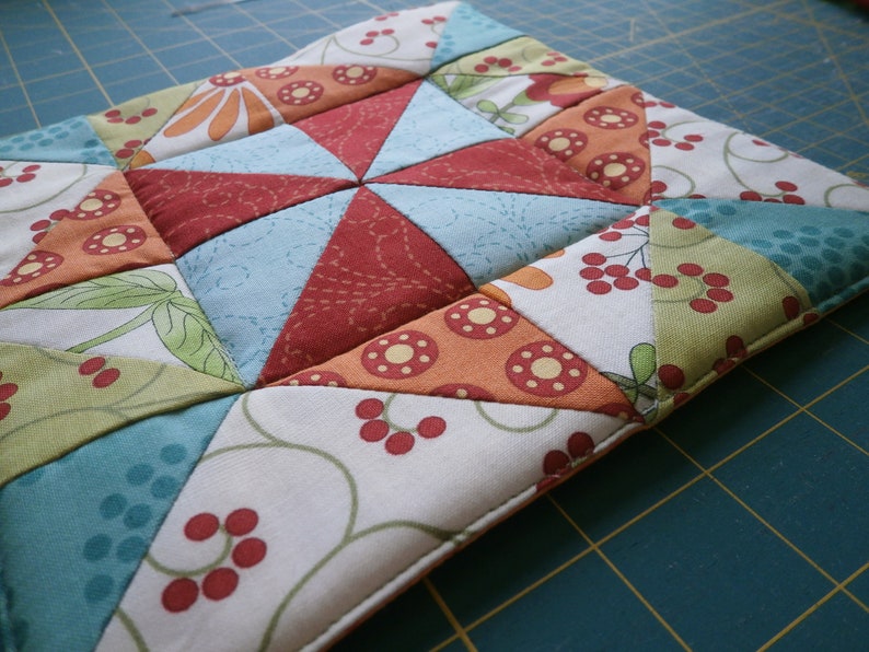 May include: A colorful patchwork quilt square with a variety of floral and geometric patterns in shades of red, green, blue, and white.