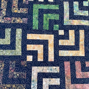 May include: A quilt featuring a dark navy blue background with a continuous swirling stitch pattern. The design consists of L-shaped blocks in various colors including green, orange, peach, and multi-colored patterns with circular motifs.