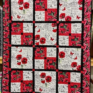 May include: A quilt with a black and red border and a white background. The quilt is made up of nine squares, each with a different design featuring red poppies, Eiffel Towers, and Parisian-themed text. The text includes "VILLE DE PARIS" and "DE PARIS".