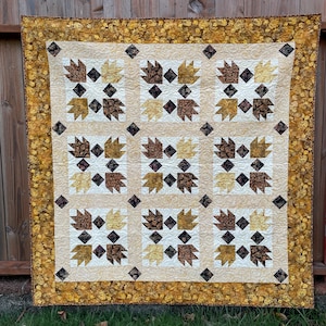 May include: A handmade quilt with a bear paw pattern. The quilt features squares of cream, brown, and gold fabrics. The border is a floral pattern in shades of gold and brown. The quilt is displayed outdoors.