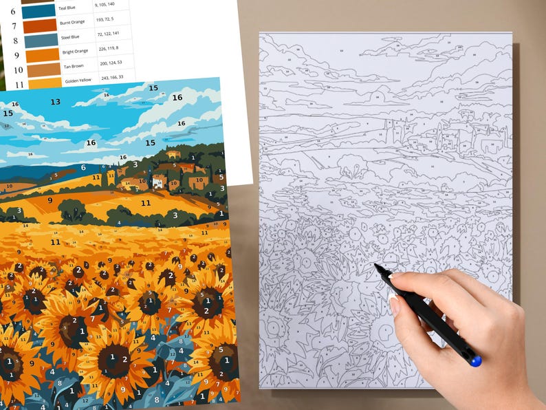 May include: A paint-by-numbers kit depicting a sunflower field and a Tuscan landscape. The kit includes a canvas with numbered sections, paint colours, and a reference sheet. A hand is shown holding a black pen, ready to paint.