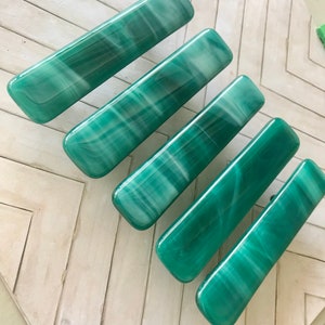 May include: Six rectangular, green malachite stone drawer pulls with white veining. The pulls are arranged diagonally on a light-colored, chevron-patterned surface. The pulls have rounded edges and a glossy finish.