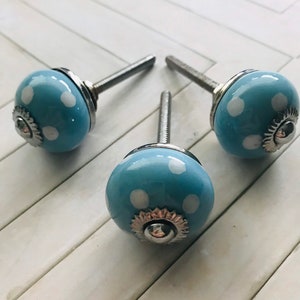 May include: Three round cabinet knobs featuring a light blue glazed finish with white polka dots. Each knob has a silver-toned metal base with a decorative scalloped edge and a threaded metal bolt extending from the back for installation purposes.