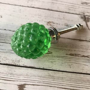 May include: A green glass cabinet knob with a textured, bubble-like design. The knob is attached to a silver metal base with a threaded rod and nut. The knob is approximately 1.5 inches in diameter.