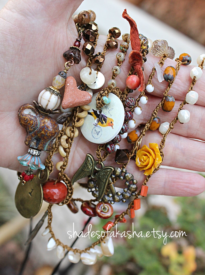Peut inclure: Plusieurs colliers faits &agrave; la main avec divers breloques et perles. Les colliers pr&eacute;sentent une vari&eacute;t&eacute; de couleurs, notamment le marron, l'orange et le blanc. Les breloques comprennent un &eacute;l&eacute;phant, un c&oelig;ur, un oiseau et des ailes d'ange. Les colliers sont pr&eacute;sent&eacute;s sur une main.