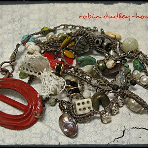 Peut inclure: Plusieurs colliers faits &agrave; la main avec diverses perles, dont des turquoises, des perles et des cristaux transparents. Les colliers sont entrelac&eacute;s avec un fermoir ovale rouge et un morceau de dentelle blanche. Le texte "robin dudley-howes" est inclus.