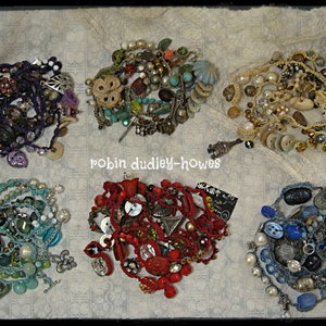 Peut inclure: Six colliers faits &agrave; la main, chacun avec un design unique. Ils pr&eacute;sentent une vari&eacute;t&eacute; de perles, boutons et breloques dans des couleurs comme le violet, le rouge, le bleu et le turquoise. Le texte "robin dudley-howes" est visible.