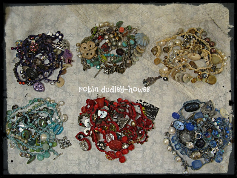 Peut inclure: Six colliers faits &agrave; la main, chacun avec un design unique. Ils pr&eacute;sentent une vari&eacute;t&eacute; de perles, boutons et breloques dans des couleurs comme le violet, le rouge, le bleu et le turquoise. Le texte "robin dudley-howes" est visible.