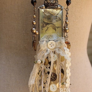 May include: A vintage-inspired necklace with a glass pendant featuring a bird illustration. The pendant is adorned with a crown and surrounded by a lace trim. The necklace also features a variety of beads, buttons, and charms.