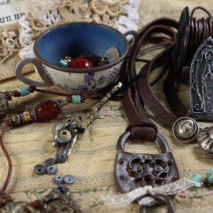 Peut inclure: Un assortiment de fournitures de fabrication de bijoux, comprenant des cordons en cuir, des perles, un cadenas d&eacute;coratif et une tasse &agrave; th&eacute; vintage remplie de perles. La palette de couleurs comprend le marron, l'argent, le bleu et le rouge.