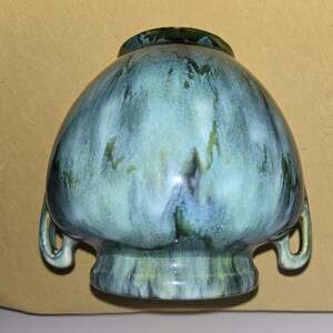 May include: A green and white glazed ceramic vase with two handles. The vase has a rounded body and a flared base.