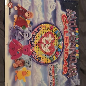 May include: A Beanie Babies Millennium Calendar, Year 2000, featuring various plush toy characters. The calendar cover has a celestial background with the words "Millennium Calendar" in a glittery font. The calendar is an authentic Ty product.