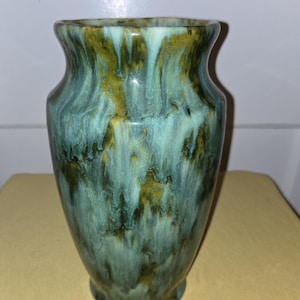 May include: A green and yellow glazed ceramic vase with a rounded body and a flared opening. The vase has a mottled, marbled effect.