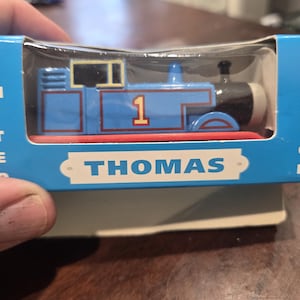 May include: A blue toy train engine labeled with the number 1 in a light blue box. The packaging features the text LIMITED EDITION on the sides and THOMAS on the front. The train has a black front section, a red base, and a yellow window frame.