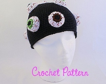 Puede incluir: Gorro de punto negro con aplicaciones de ojos blancos y verdes. Patrón de ganchillo.