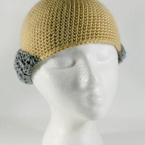 May include: A beige crocheted beanie with gray crocheted ear flaps. The beanie is on a white mannequin head.